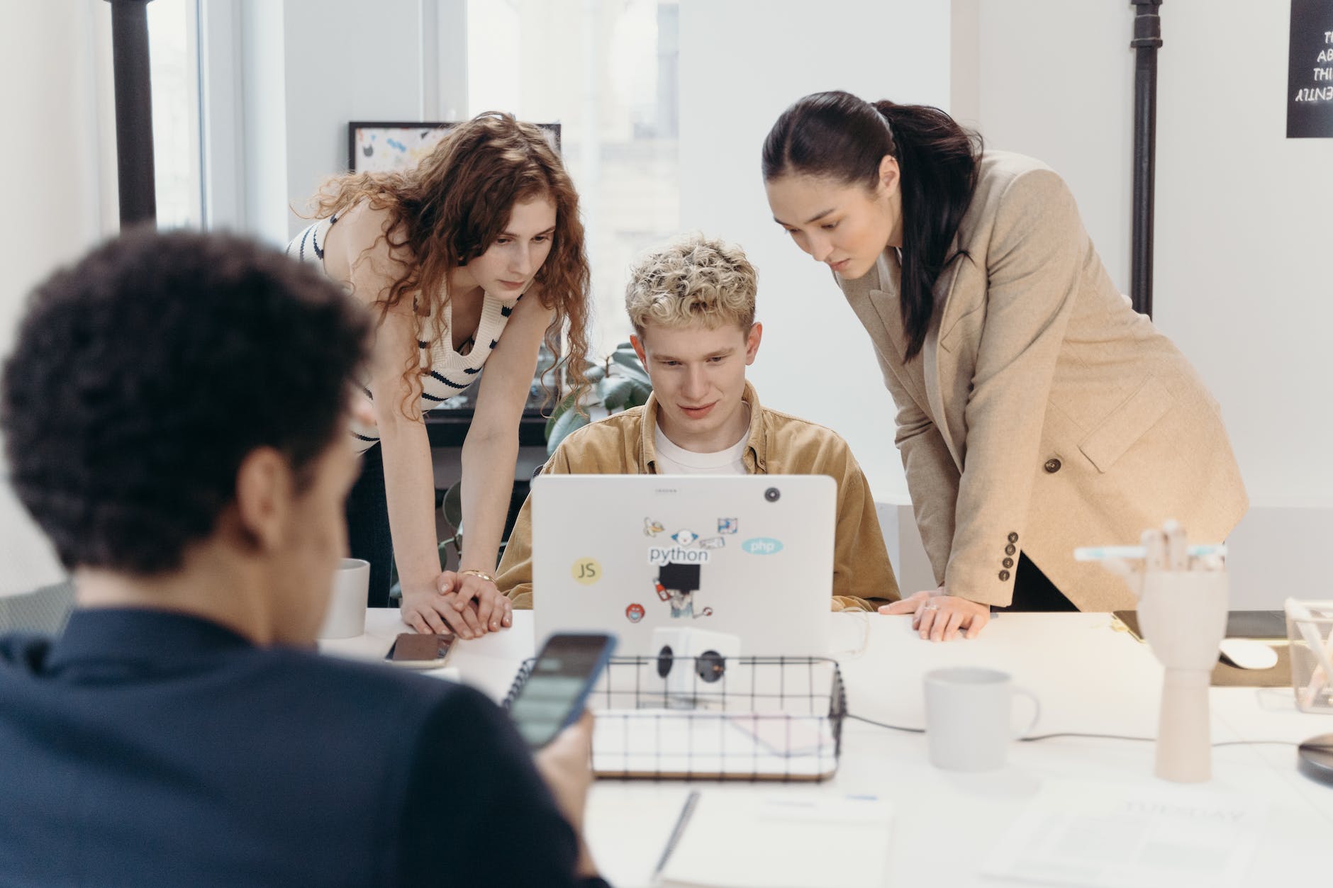women standing beside a man using a laptop