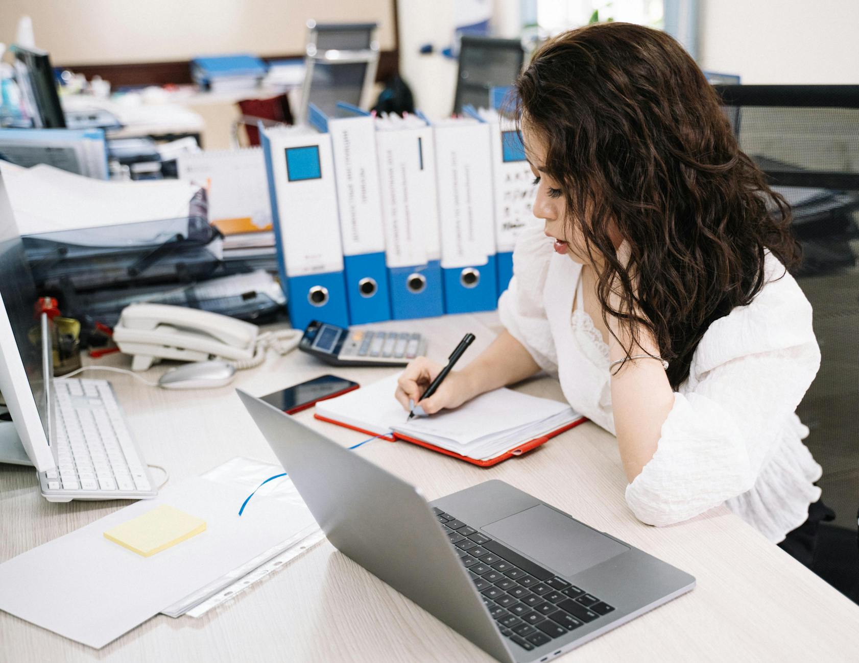 woman writing on notebook while using laptop